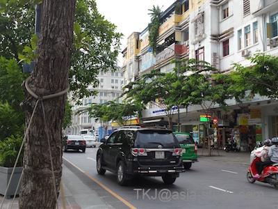 ホーチミン市中心部の並木道と走る車、路肩にバイクが並ぶ街角風景