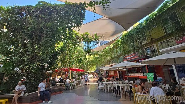 緑に囲まれた中庭のフードコート全景、テーブル席と店が並ぶ