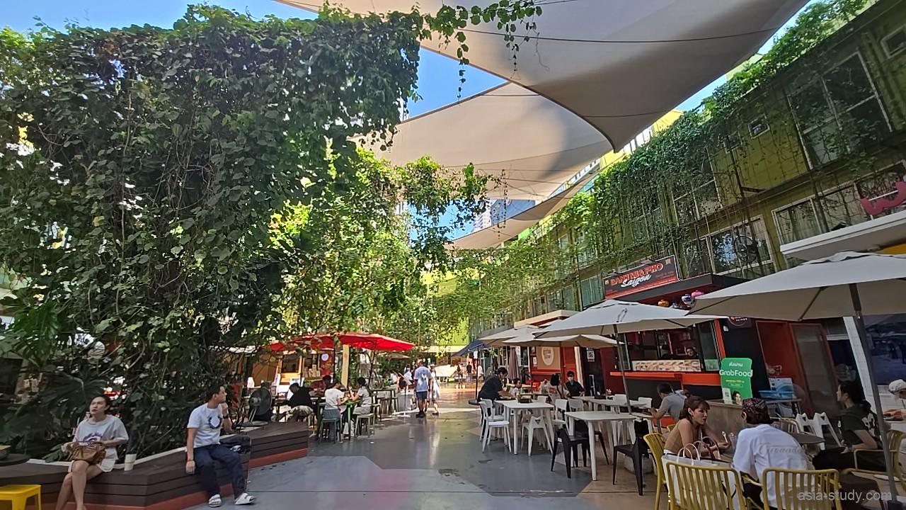 緑に囲まれた中庭のフードコート全景、テーブル席と店が並ぶ