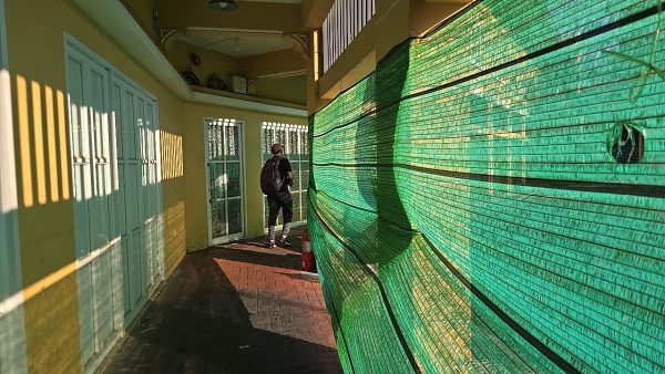 緑の工事ネット沿いに曲がる細い通路、夕日で影が伸びる