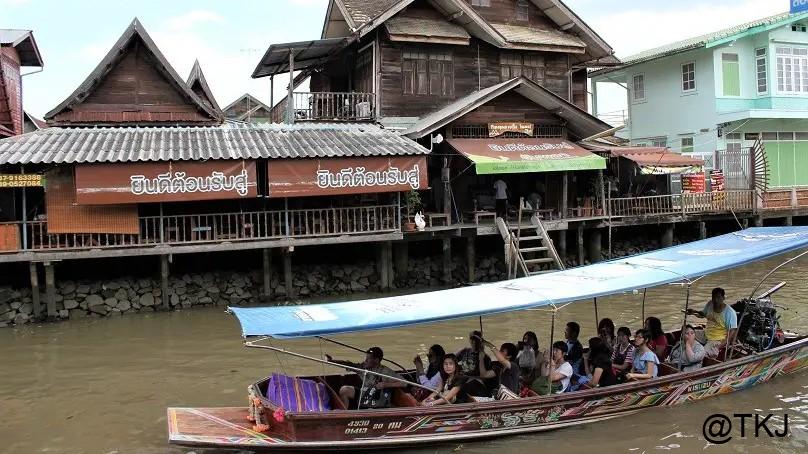 水上マーケットの運河を走るボート、川沿いの木造家屋と観光客が乗る船の様子