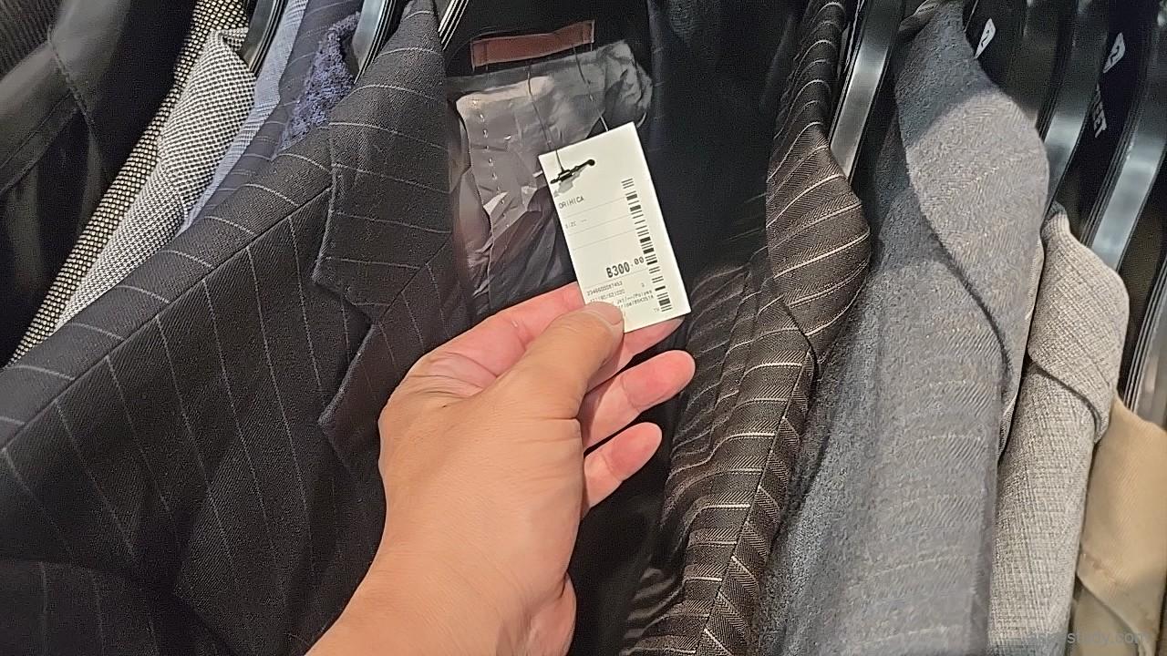 ジャケット売り場で値札を確認する手元、ラックに並ぶ上着