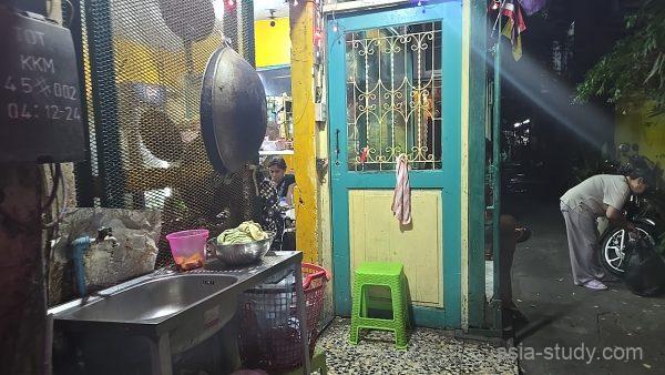 黄色の壁とエメラルドグリーンのドアが特徴的な民家、路地裏でバイクを整備する現地の人の姿