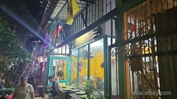 タイ国旗が掲げられた黄色い建物の外観、夜の路地で食事を楽しむ人々の風景