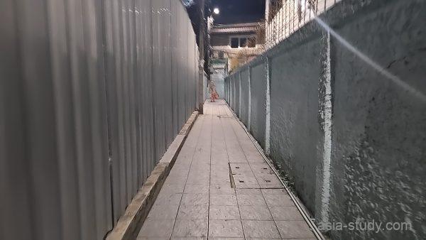 トタンの囲いとコンクリート壁に挟まれた、ひたすら続く夜の細い通路