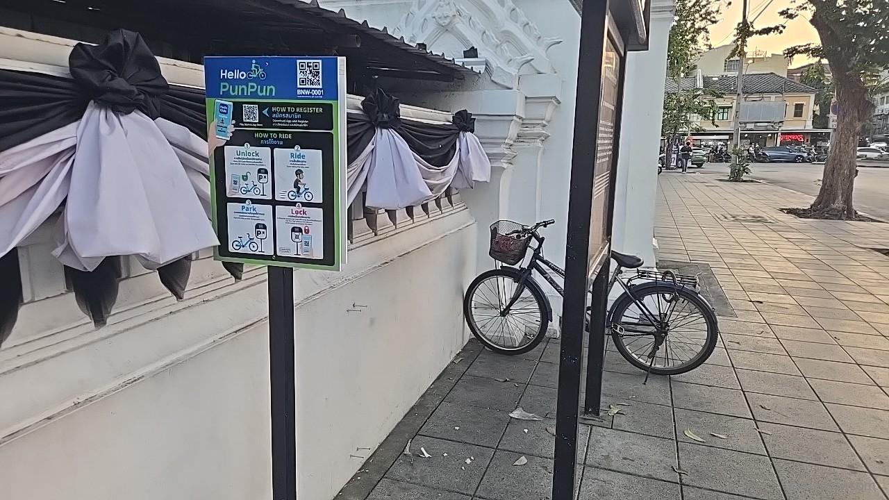 自転車シェア「Hello PunPun」の利用案内看板と、壁沿いに停めた自転車