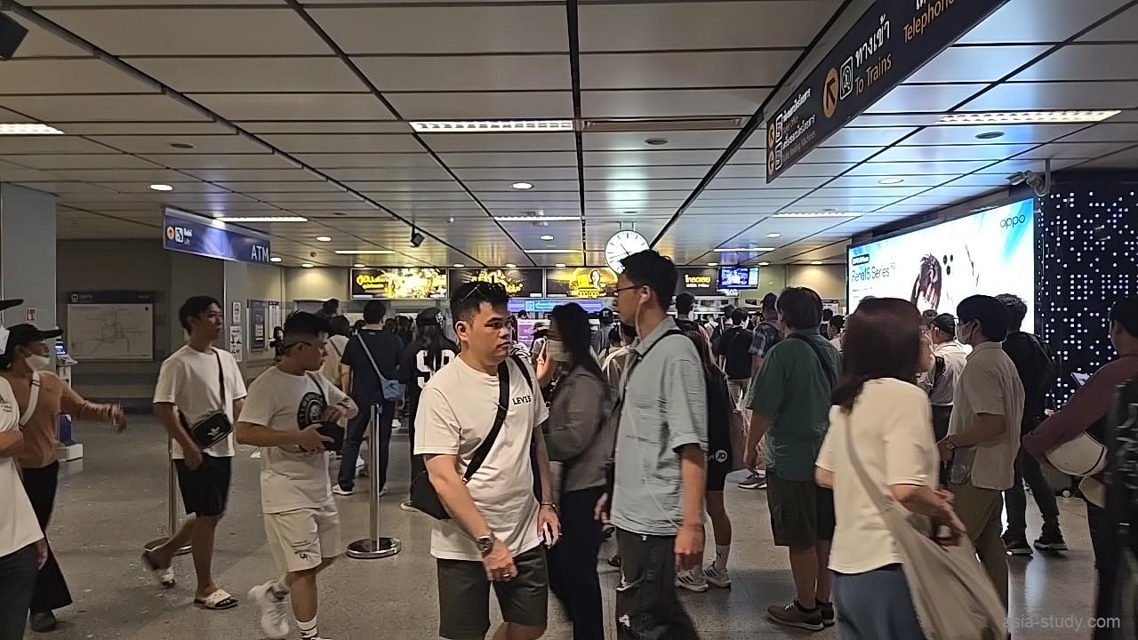 MRT駅構内の通路と行列、天井の大きな時計が見える待ち合わせエリア