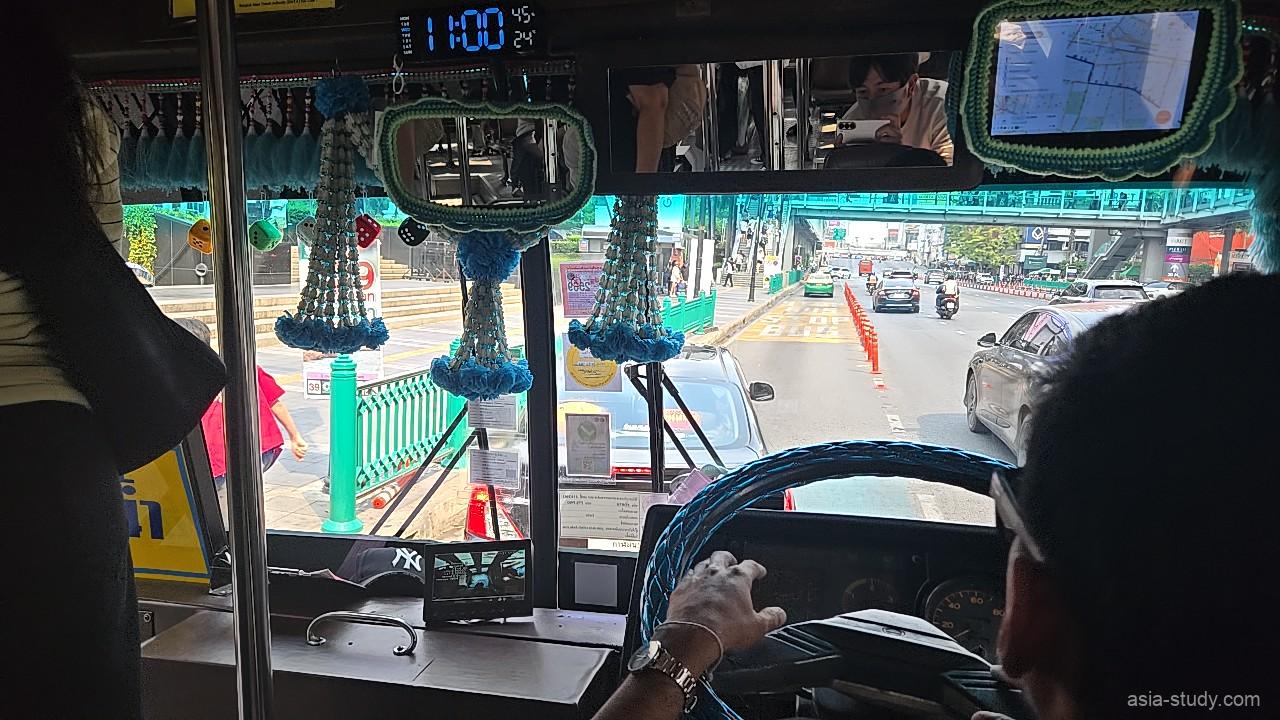 バス運転席越しの前方車窓、車内の飾りと渋滞気味の幹線道路（バンコク）
