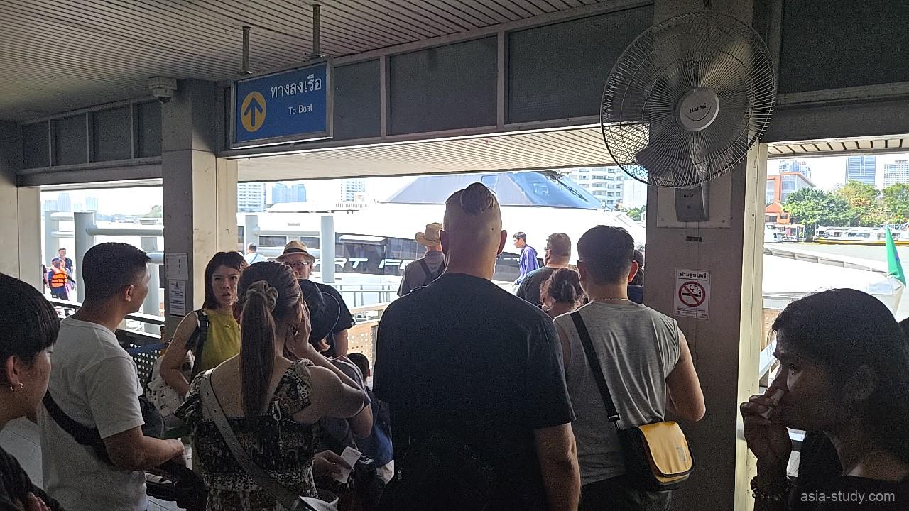 サトーン・ピアの乗船待機エリア、ワット・アルン方面へのボートを待つ多くの旅行者と案内板がある風景