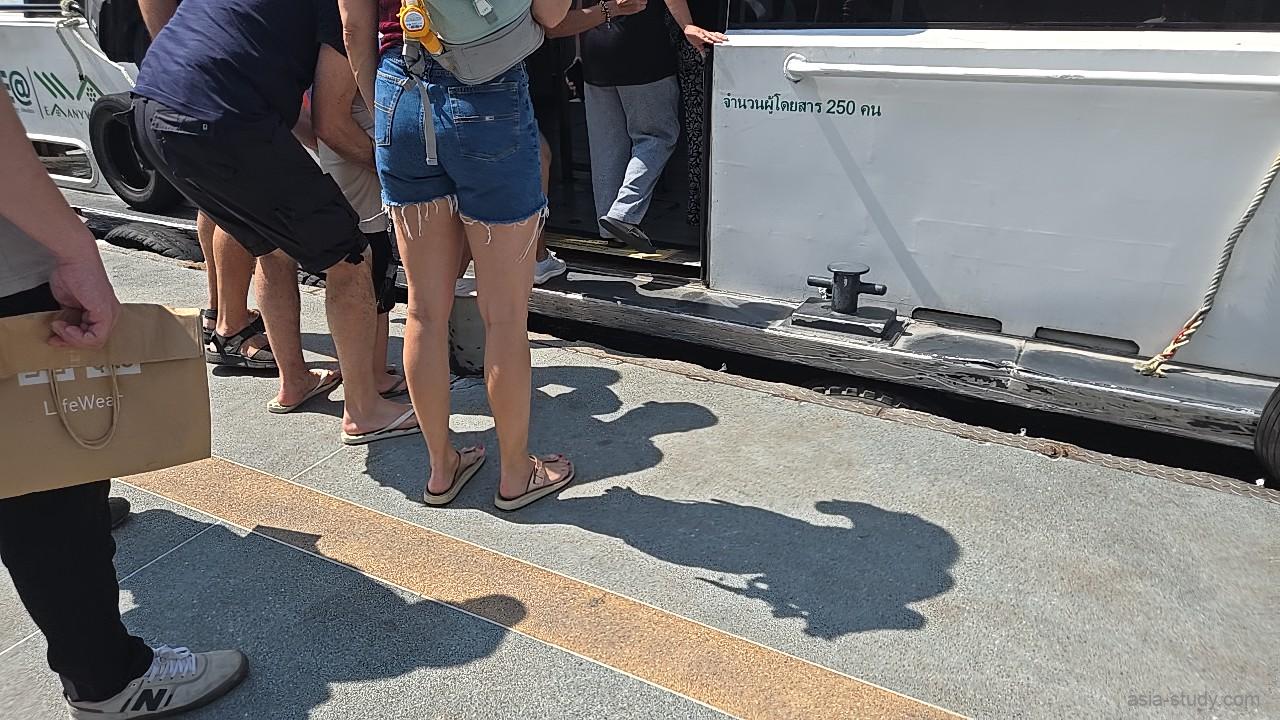 船着き場の桟橋から、チャオプラヤー・エクスプレス・ボートへ足元に注意しながら乗り込む乗客たちの様子