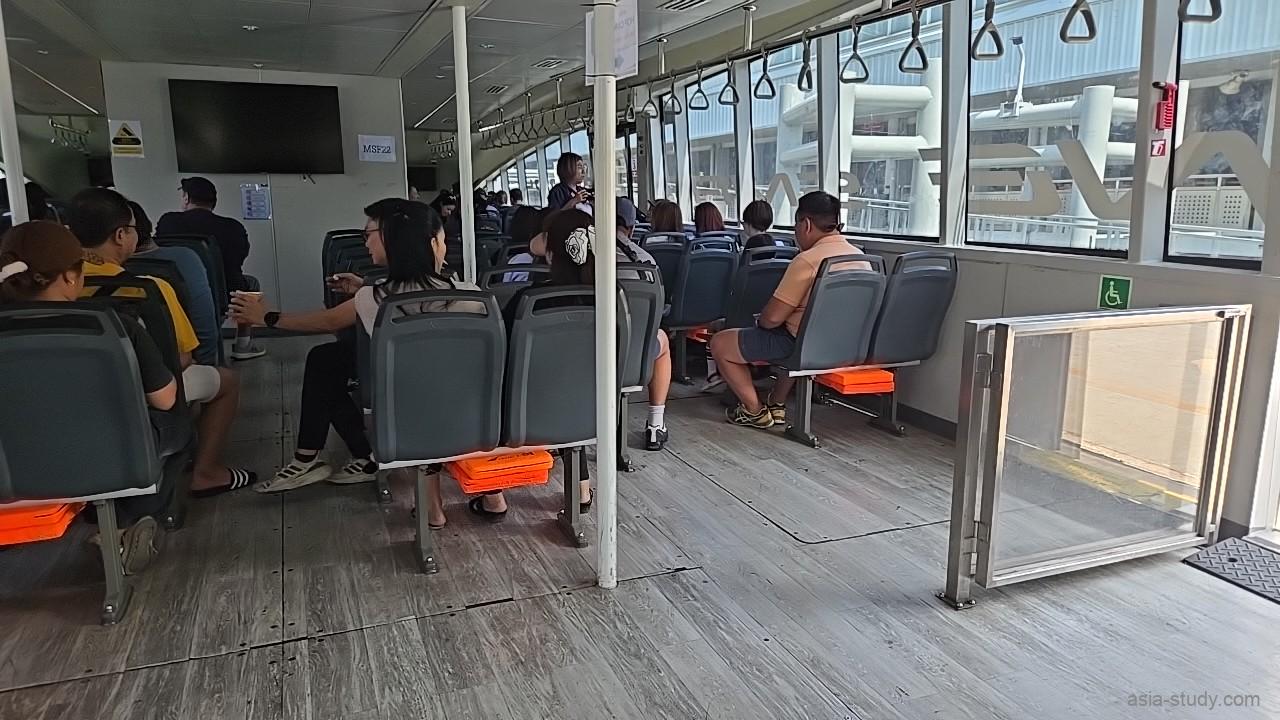 冷房の効いた快適なフェリー船内、大きな窓からチャオプラヤー川の景色を眺める乗客たちの様子