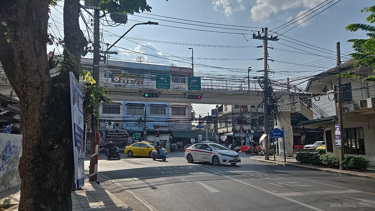 歩道橋が架かる大きな交差点、黄色いタクシーやバイクが走るワット・アルンからMRT駅へ向かう道中の風景