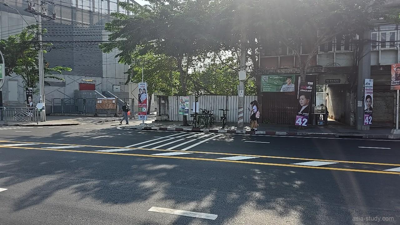 選挙ポスターが並ぶバンコクの路上、横断歩道の手前にある Anywheel のレンタル自転車置き場付近