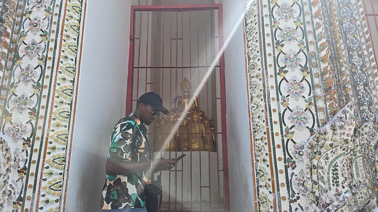 金網の奥に安置された金色の仏像の前に立つ、サングラスをかけた観光客の男性