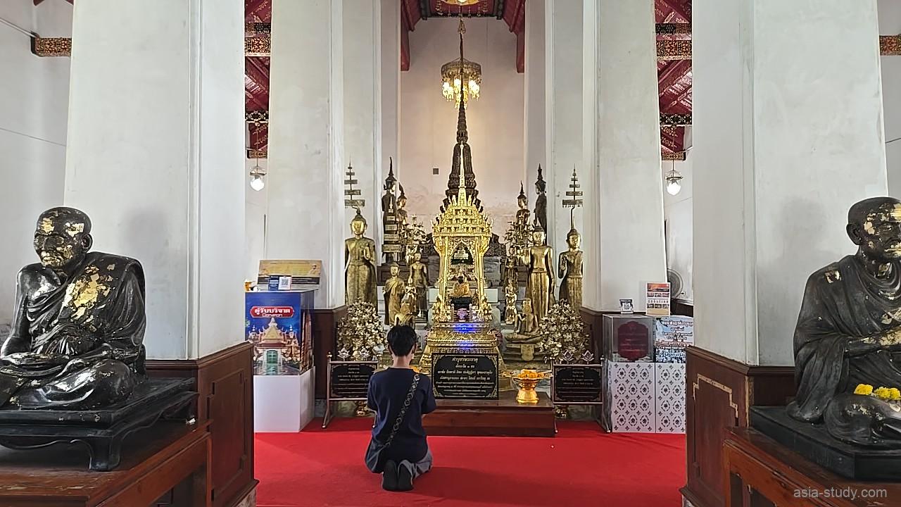 金色の装飾が施された高い尖塔状の供養塔の前で、熱心に祈りを捧げる参拝客の後ろ姿