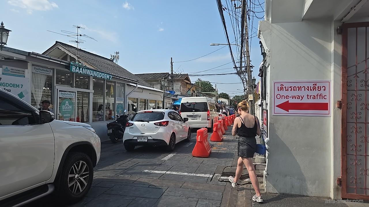 ワット・アルン西出口付近の一方通行路、マツダ車などの白い乗用車が走り、右側の壁には赤い矢印の「One-way traffic」の標識がある風景