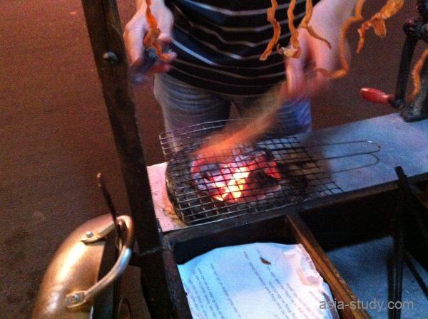 路上の炭火コンロで串を焼く様子、煙が上がる屋台のグリル台