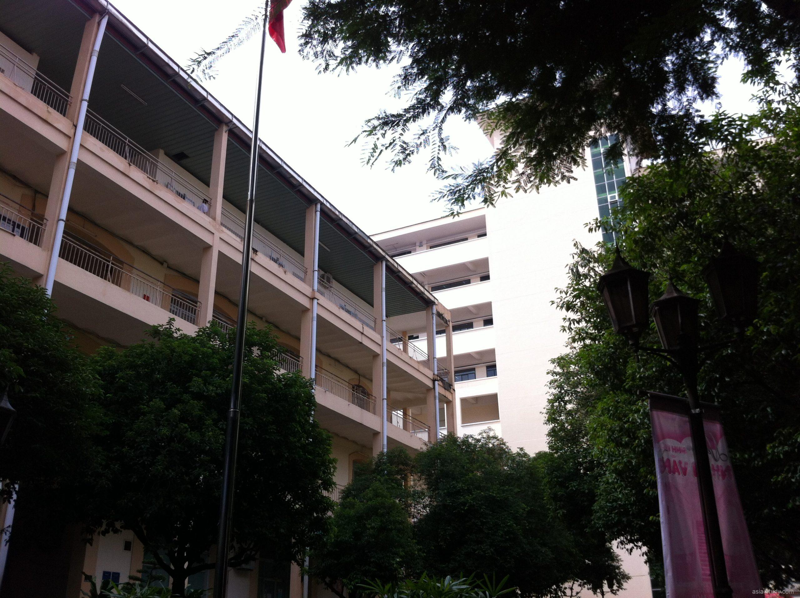 校舎の中庭に立つ旗竿と、ベージュ色の校舎（木々に囲まれたキャンパス風景）