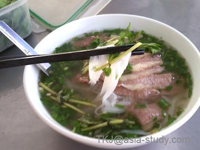 フォーに白ねぎと牛肉をのせて食べる様子（箸で麺を持ち上げ）