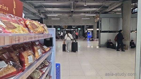 スワンナプーム空港の通路、ベーカリー棚の横をスーツケースで移動する旅行者