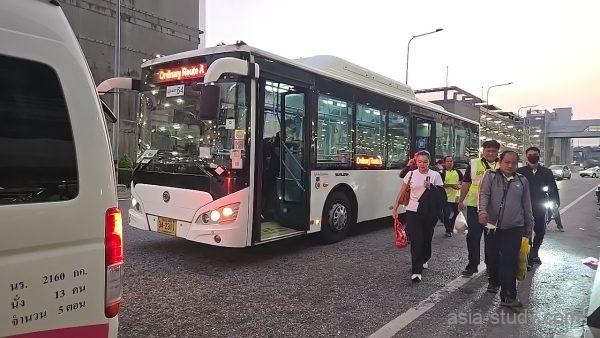 スワンナプーム空港の路線バス前、降車して歩く人々（夕景）