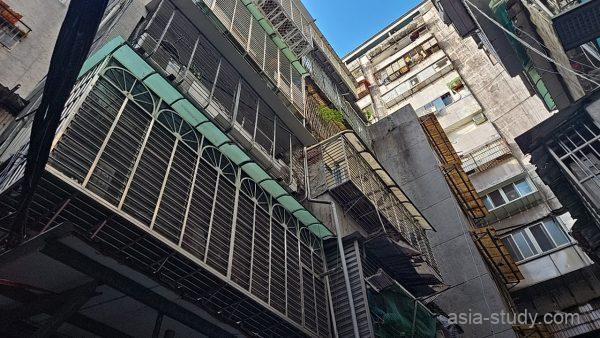 台北・龍山寺周辺の古い集合住宅を見上げた路地風景（鉄格子バルコニーが並ぶ建物）