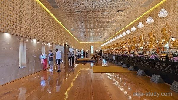 長い礼拝ホールにずらっと並ぶ金色の仏像列（シャンデリアと光沢床）