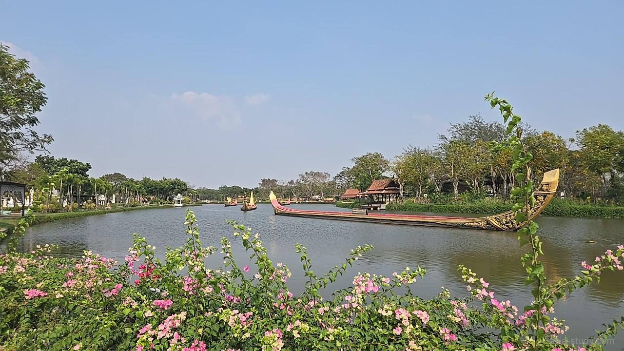 湖に浮かぶ長い船と、手前のピンクの花（アンシエント・シティ）