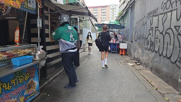 路地の屋台と通行人、壁一面の落書きがあるバンコクの裏通り風景