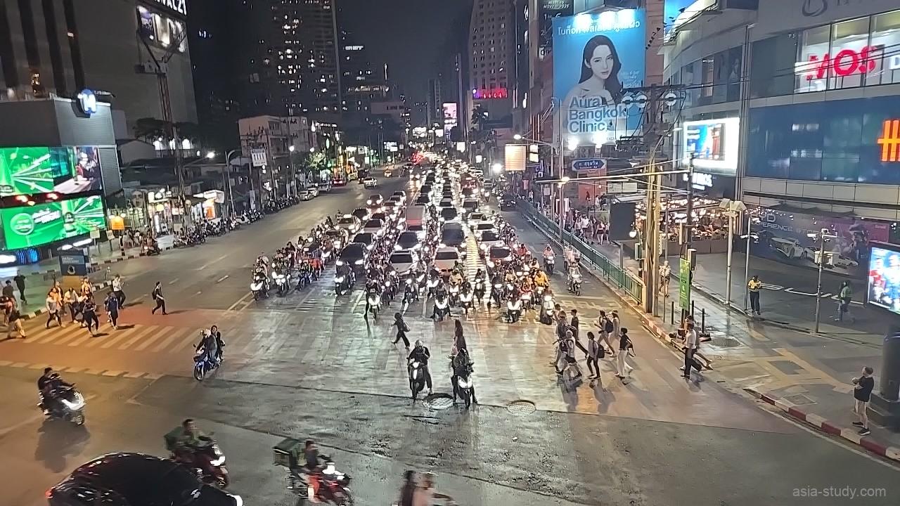 夜の大通りでバイクと車が連なり、横断歩道を人が渡るバンコクの交差点