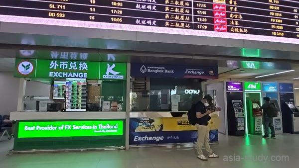 空港内の両替カウンターとATM、上部にフライト案内板がある通路の様子