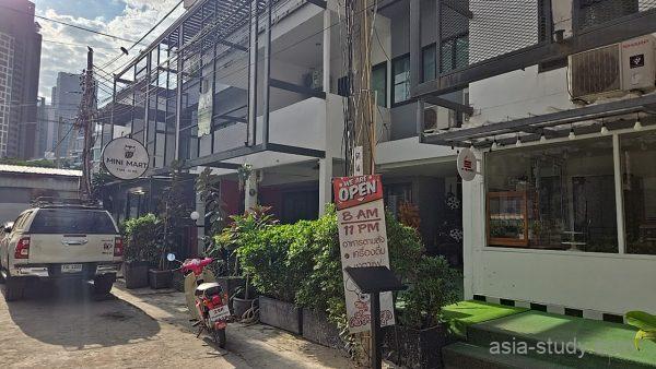 ゲストハウス前の路地と入口、ミニマート看板と「OPEN 8AM-11PM」の掲示