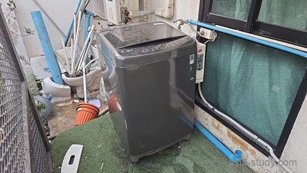 屋外の洗濯機スペース、配管とホースが見える洗濯エリア
