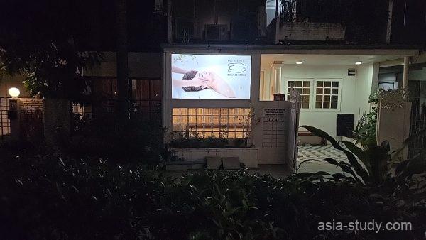 夜の中庭と建物外観、明るい看板が光るゲストハウス入口